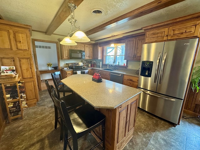 kitchen with brown cabinetry, stainless steel appliances, a textured ceiling, beamed ceiling, and a center island