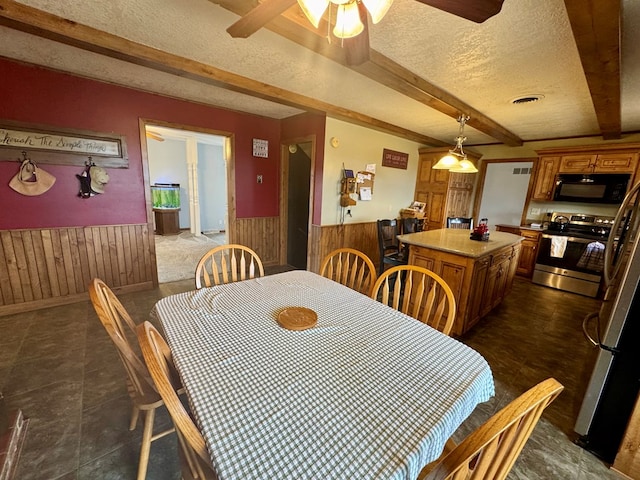 dining area featuring visible vents, a wainscoted wall, wood walls, beam ceiling, and a textured ceiling