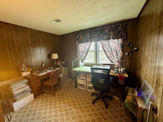 carpeted office featuring visible vents, wood walls, and a textured ceiling