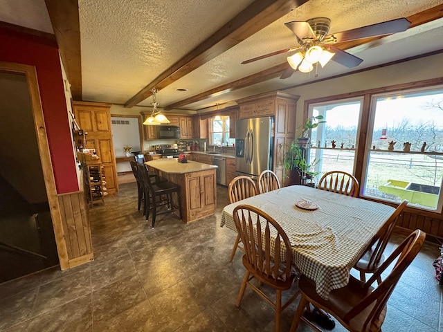 dining space with ceiling fan, beamed ceiling, wainscoting, and a textured ceiling