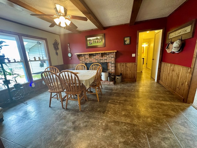 dining area with a wainscoted wall, beamed ceiling, wood walls, a fireplace, and a textured ceiling