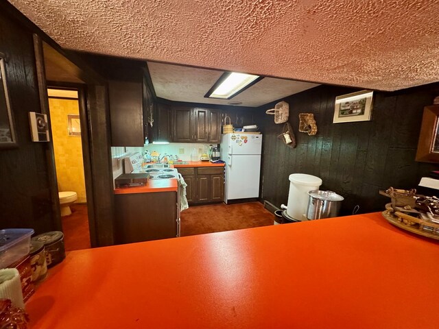 kitchen with a sink, a textured ceiling, freestanding refrigerator, wood walls, and light countertops