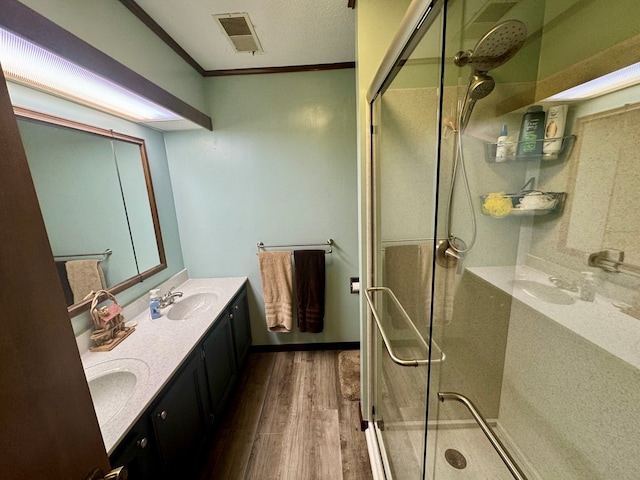 bathroom featuring visible vents, ornamental molding, wood finished floors, a shower stall, and double vanity