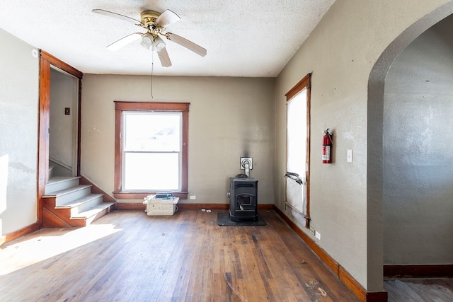 interior space with a textured ceiling, ceiling fan, dark hardwood / wood-style flooring, and a wood stove