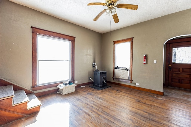 foyer entrance with ceiling fan, wood-type flooring, a wood stove, and a textured ceiling