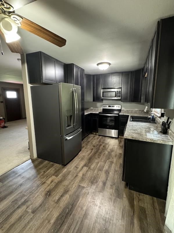 kitchen with light stone countertops, stainless steel appliances, ceiling fan, dark wood-type flooring, and sink