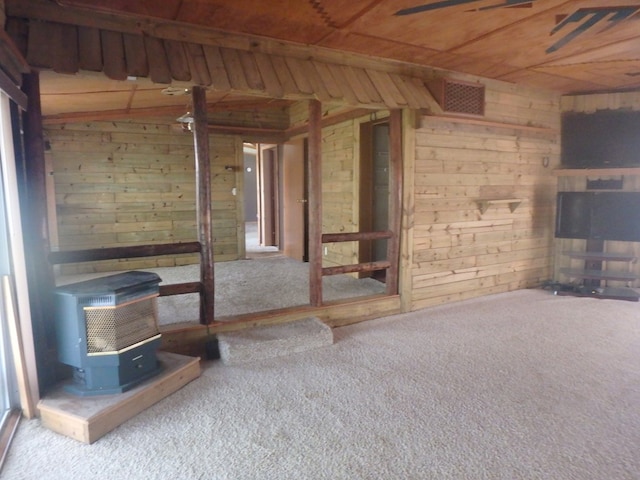 unfurnished living room with carpet floors, a wood stove, wood ceiling, and wooden walls