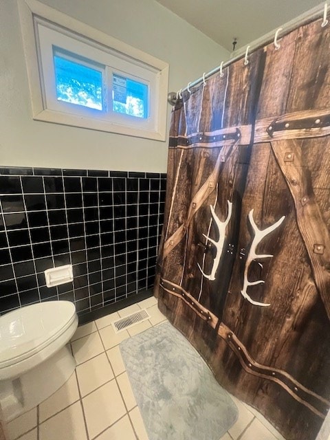 bathroom with toilet, tile patterned floors, and tile walls