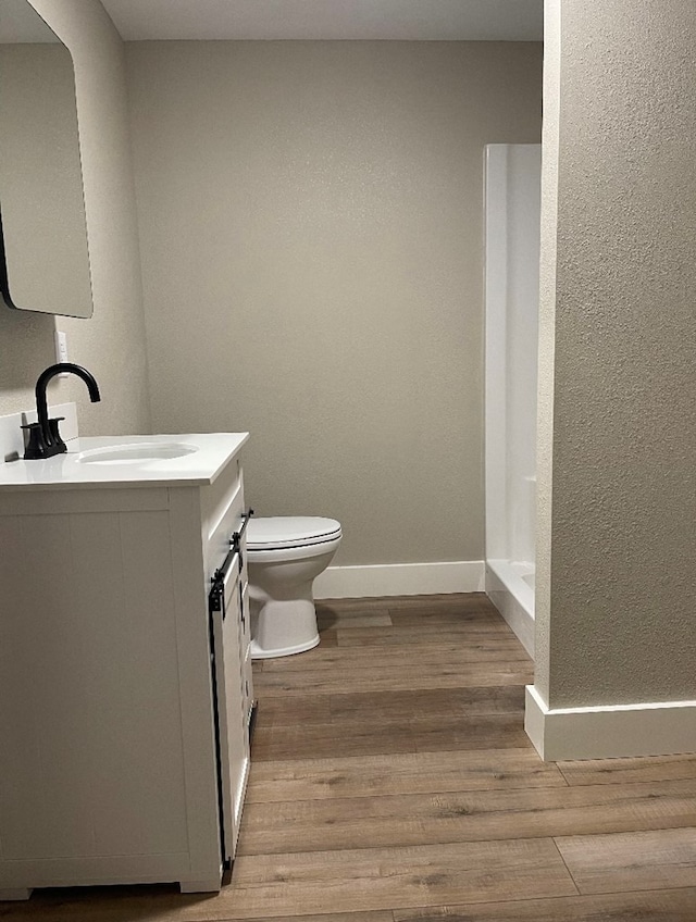 bathroom with hardwood / wood-style flooring, vanity, toilet, and a shower