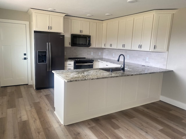 kitchen with black appliances, sink, light stone counters, kitchen peninsula, and light hardwood / wood-style flooring