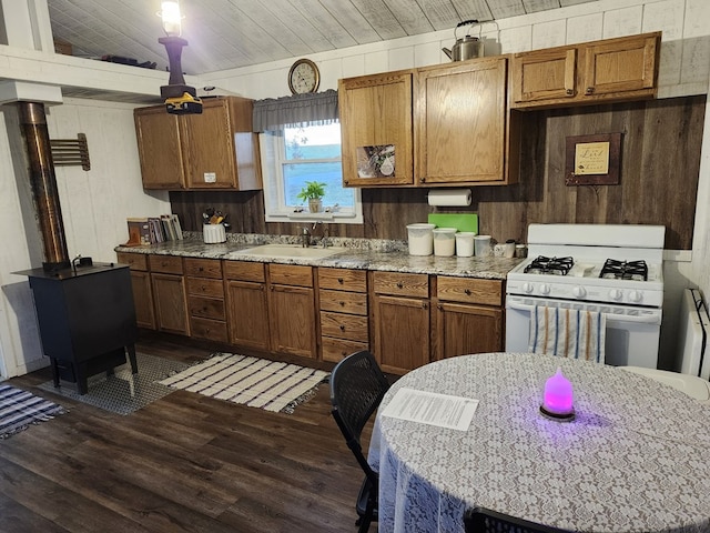 kitchen featuring white gas range oven, dark wood-type flooring, wood walls, and sink