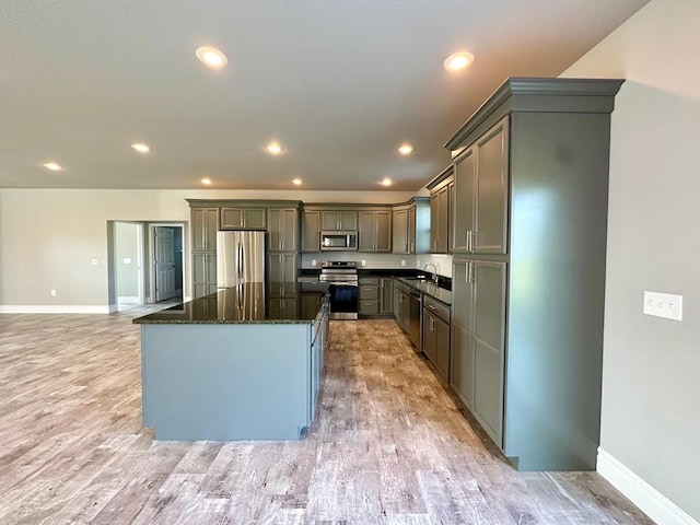 kitchen featuring a center island, dark stone counters, gray cabinets, appliances with stainless steel finishes, and light wood-type flooring