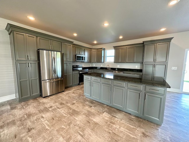 kitchen featuring gray cabinetry, a kitchen island, stainless steel appliances, and dark stone counters