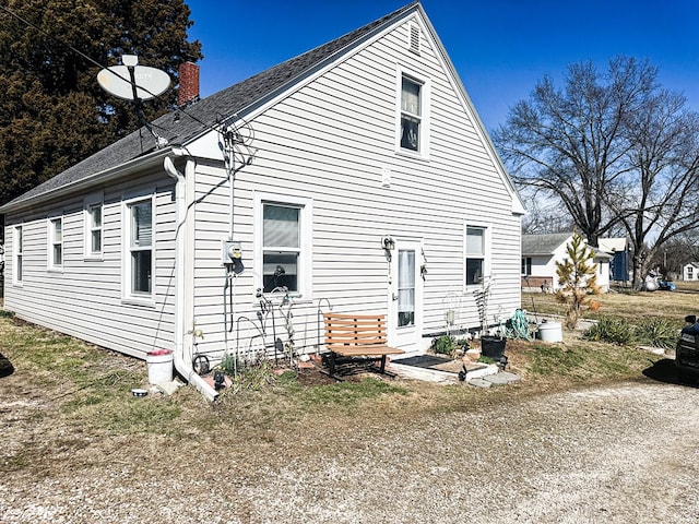 back of house featuring a chimney and a shingled roof