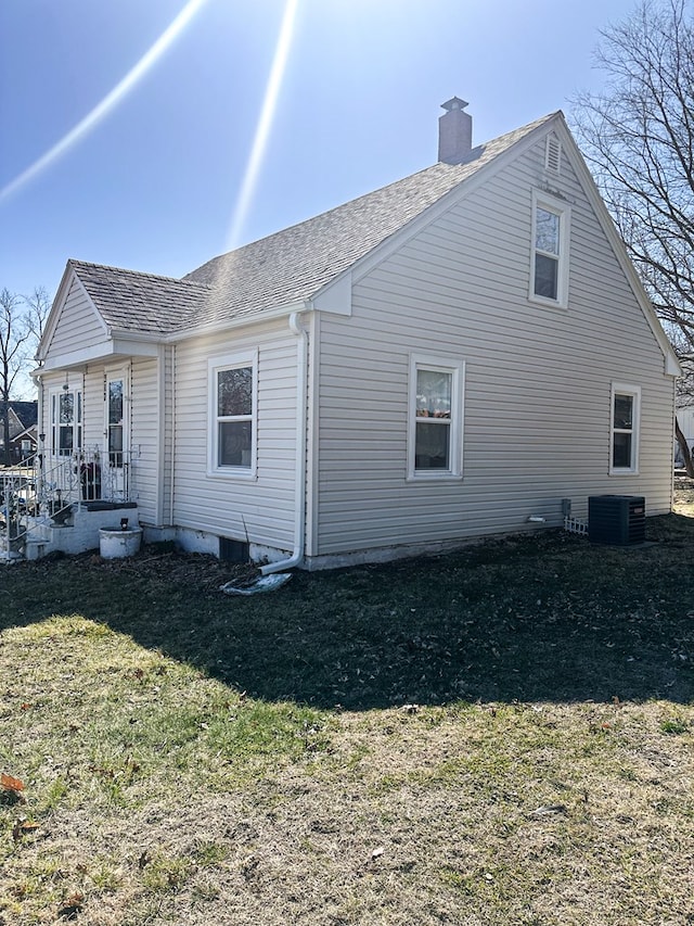 view of property exterior with a yard, central air condition unit, roof with shingles, and a chimney