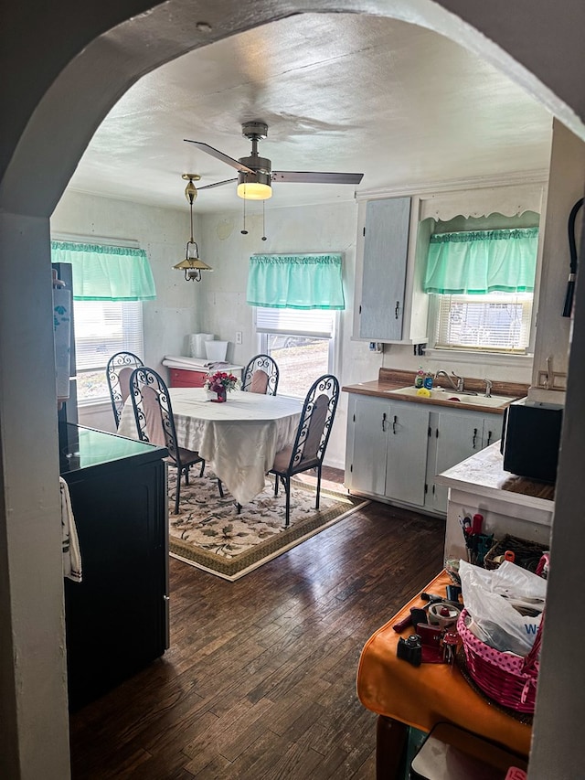 kitchen featuring a healthy amount of sunlight, a ceiling fan, arched walkways, a sink, and dark wood-type flooring