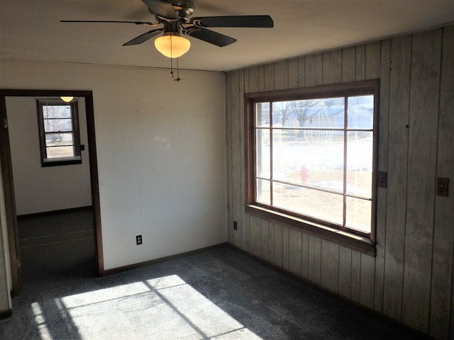 unfurnished room with wooden walls, ceiling fan, and dark colored carpet