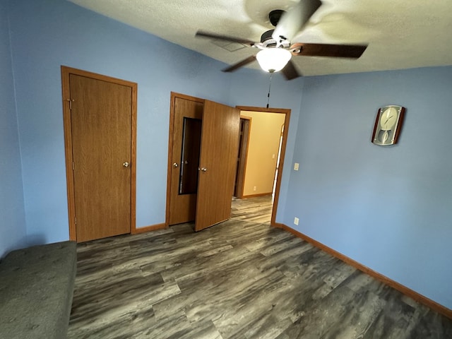 unfurnished bedroom featuring ceiling fan, dark hardwood / wood-style flooring, a textured ceiling, and multiple closets