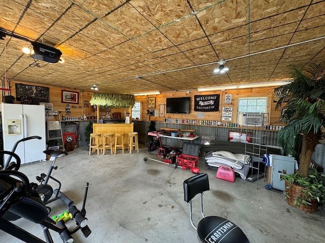 garage with a workshop area, cooling unit, white refrigerator with ice dispenser, a garage door opener, and wood walls