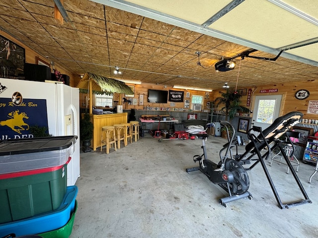 garage with a garage door opener, wooden walls, and white refrigerator with ice dispenser