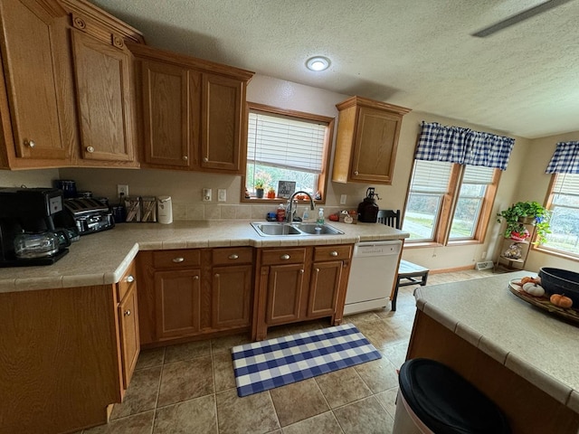 kitchen featuring tile countertops, dishwasher, sink, a textured ceiling, and light tile patterned flooring