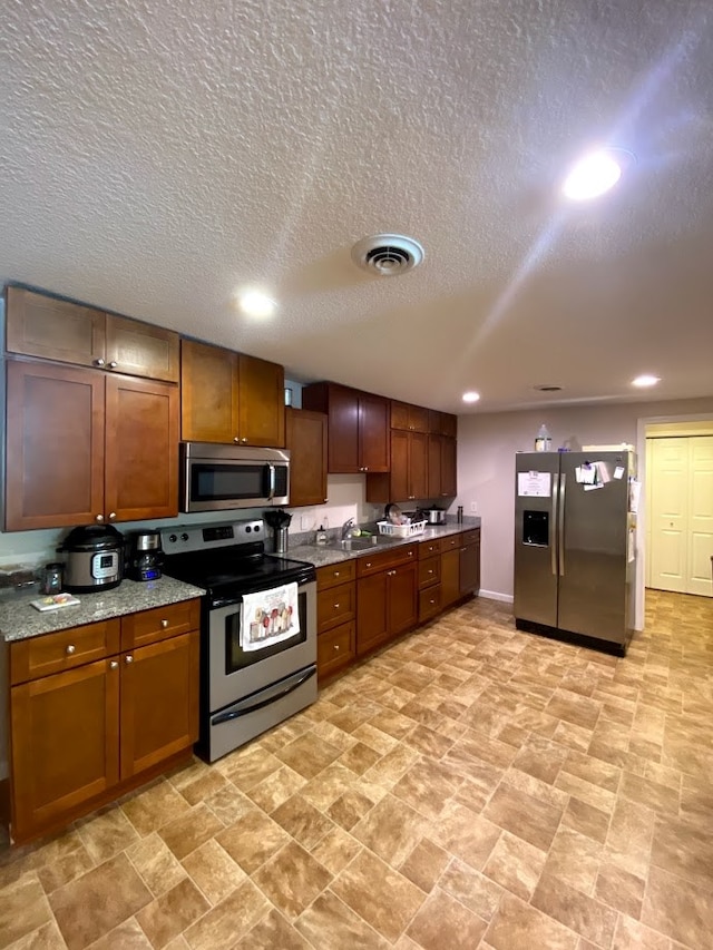 kitchen featuring a textured ceiling, sink, light stone counters, and stainless steel appliances