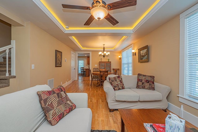 living room featuring ceiling fan with notable chandelier, light hardwood / wood-style floors, a raised ceiling, and ornamental molding