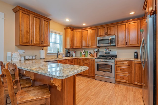 kitchen featuring sink, kitchen peninsula, a kitchen bar, appliances with stainless steel finishes, and light wood-type flooring