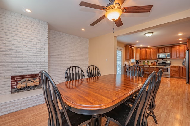 dining space with ceiling fan, light hardwood / wood-style floors, brick wall, and a brick fireplace