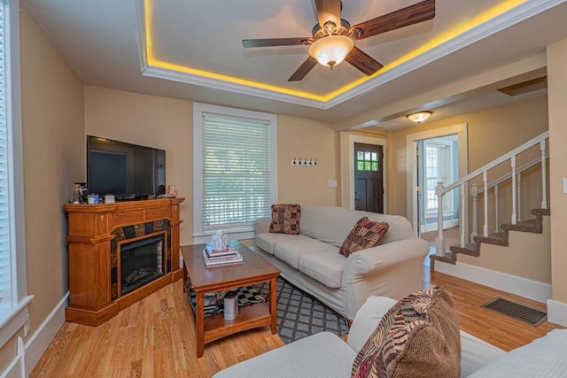 living room with a healthy amount of sunlight, light hardwood / wood-style flooring, a high end fireplace, and a tray ceiling