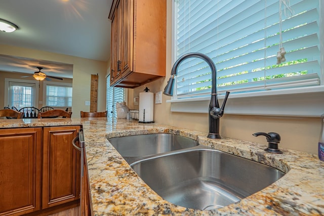 kitchen with ceiling fan, light stone counters, and sink