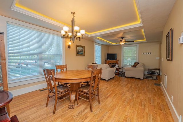 dining room featuring ceiling fan with notable chandelier, a raised ceiling, light wood-type flooring, and ornamental molding