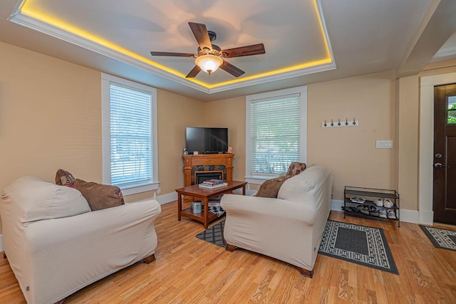 living room with a tray ceiling, light hardwood / wood-style flooring, ceiling fan, and a healthy amount of sunlight