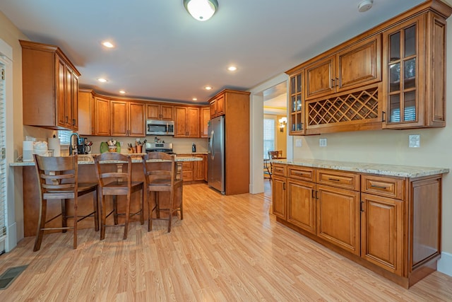 kitchen with light stone countertops, sink, stainless steel appliances, a kitchen breakfast bar, and light hardwood / wood-style floors