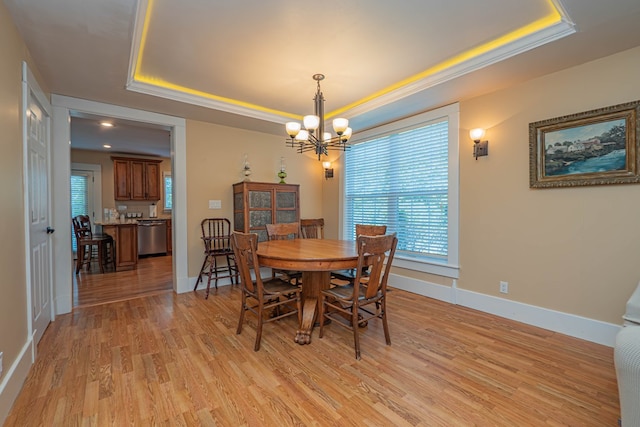 dining room featuring a raised ceiling, crown molding, light hardwood / wood-style flooring, and an inviting chandelier