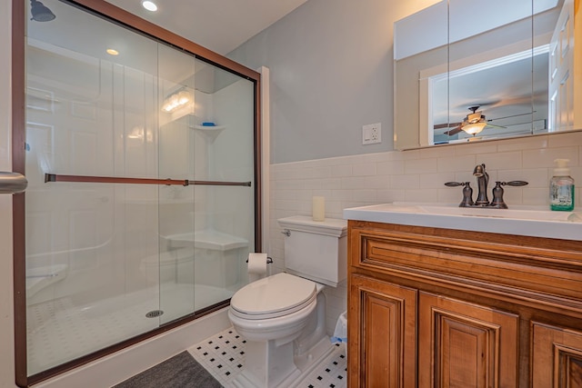 bathroom featuring ceiling fan, tile patterned floors, toilet, a shower with door, and tile walls