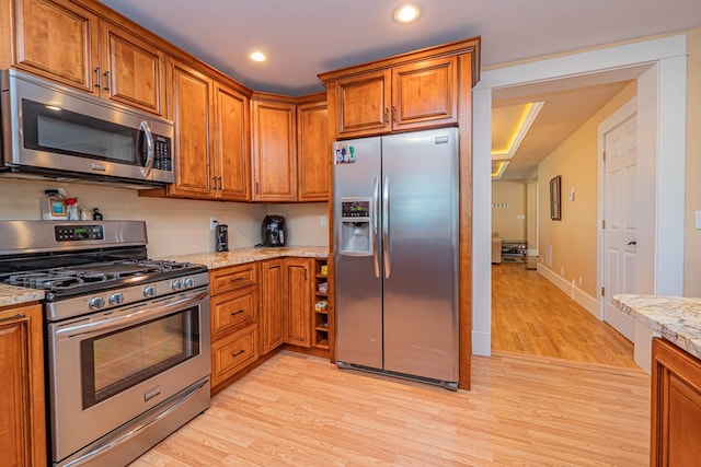 kitchen with light stone countertops, light wood-type flooring, and appliances with stainless steel finishes