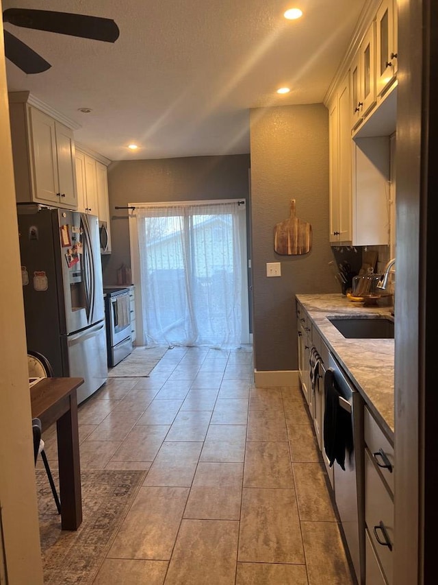 kitchen with white cabinets, sink, ceiling fan, light stone countertops, and stainless steel appliances