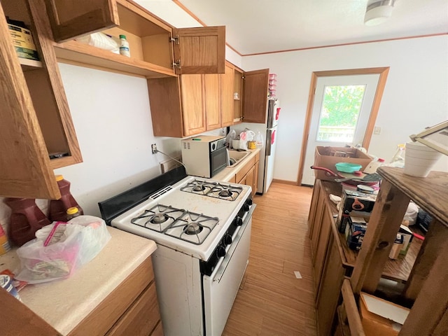 kitchen with crown molding, white gas stove, fridge, and light wood-type flooring