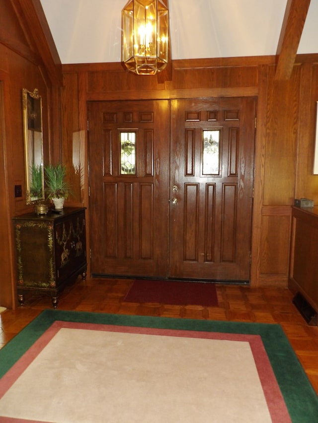 foyer with wooden walls, dark parquet floors, beamed ceiling, and an inviting chandelier