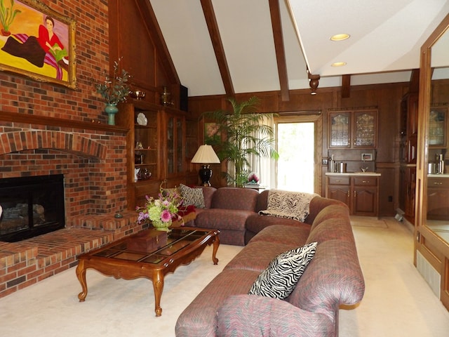 carpeted living room with beamed ceiling, high vaulted ceiling, a brick fireplace, and wood walls