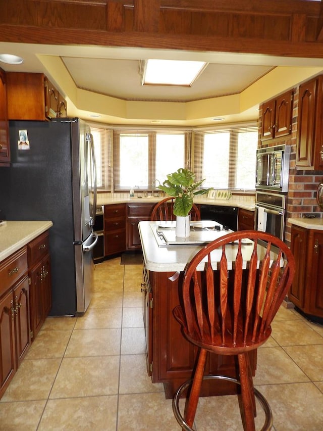 kitchen featuring sink, light tile patterned floors, appliances with stainless steel finishes, a kitchen island, and a breakfast bar area