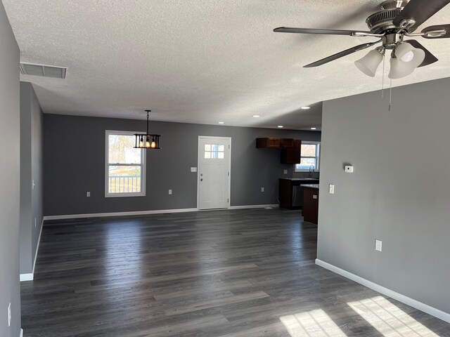 unfurnished living room with ceiling fan with notable chandelier, dark wood-type flooring, a textured ceiling, and a wealth of natural light