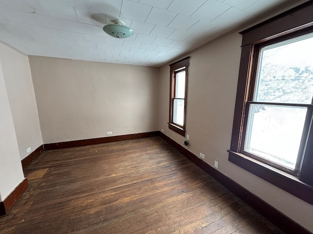 empty room featuring ornamental molding, dark wood-style flooring, and baseboards