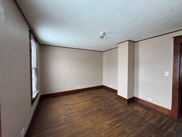 unfurnished room with ornamental molding, dark wood finished floors, and baseboards