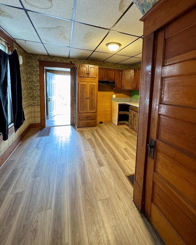 kitchen with light wood-type flooring, brown cabinets, a paneled ceiling, and under cabinet range hood