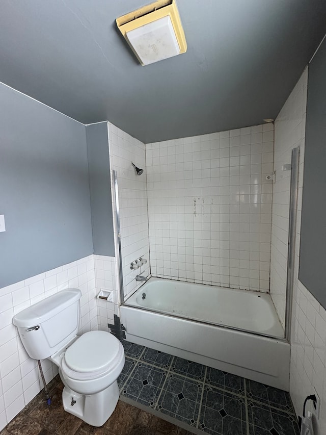 full bathroom featuring shower / bathtub combination, tile patterned flooring, toilet, tile walls, and wainscoting