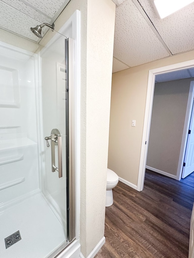 bathroom with wood-type flooring, toilet, a drop ceiling, and a shower with shower door