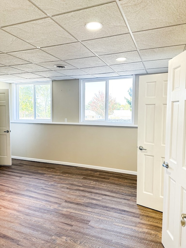 empty room with plenty of natural light, a drop ceiling, and dark wood-type flooring