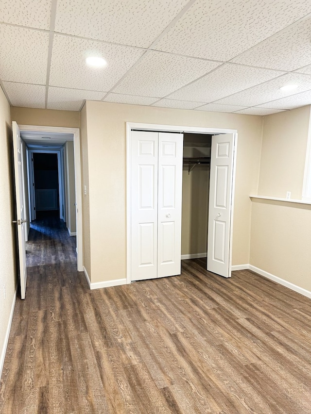 unfurnished bedroom with a paneled ceiling, a closet, and dark hardwood / wood-style flooring